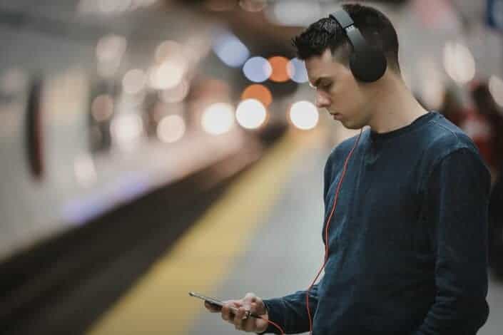Young guy wearing headphones checking on his phone while waiting for the train to arrive