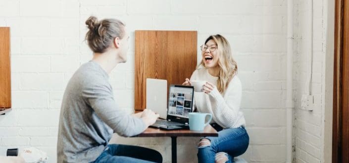 A guy and lady laughing about something, enjoying their coffee while working