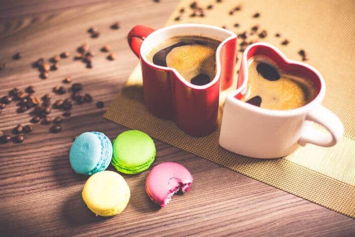 Heart-shaped mugs with coffee beans and four macarons.