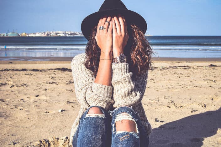 Girl in a beach covering her face with her hands.