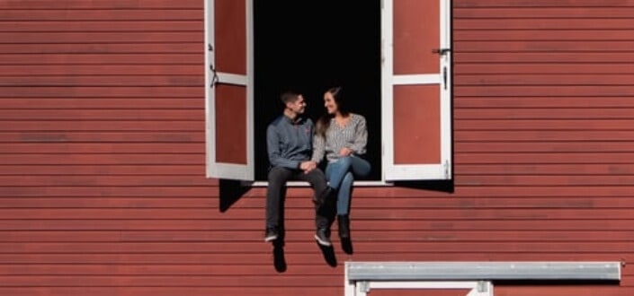 Couple sitting on window of red barn