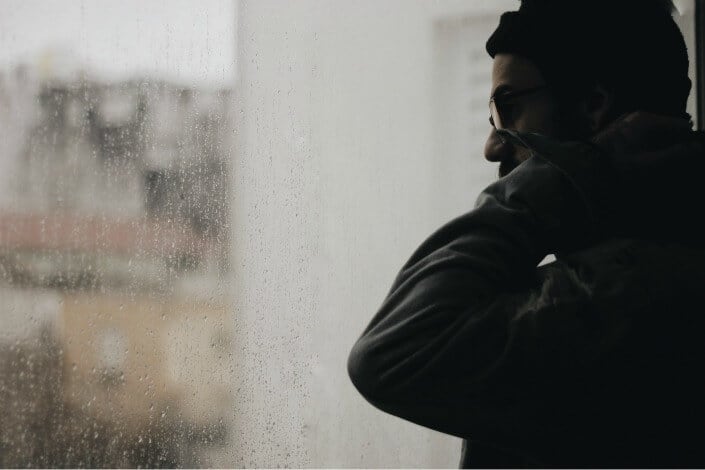 Melancholic guy staring outside a rainy window