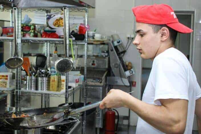 Guy in red hat cooking and about to toss food