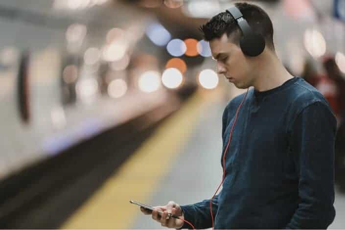 A young man with headphones looking at his phone waiting for the train to arrive