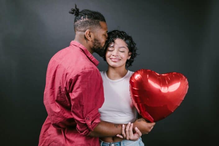 man-kissing-his-woman-while-holding-a-red-heart-shaped-balloon-