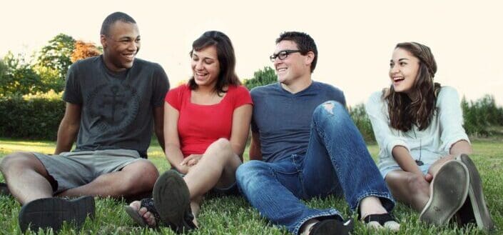 smiling-women-and-men-sitting-on-green-grass-