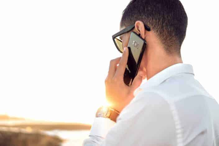 Man with a white long sleeves and heavy glasses talking to someone over his phone