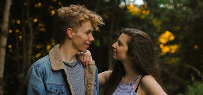 couple talking in the woods while woman is holding on man's shoulder