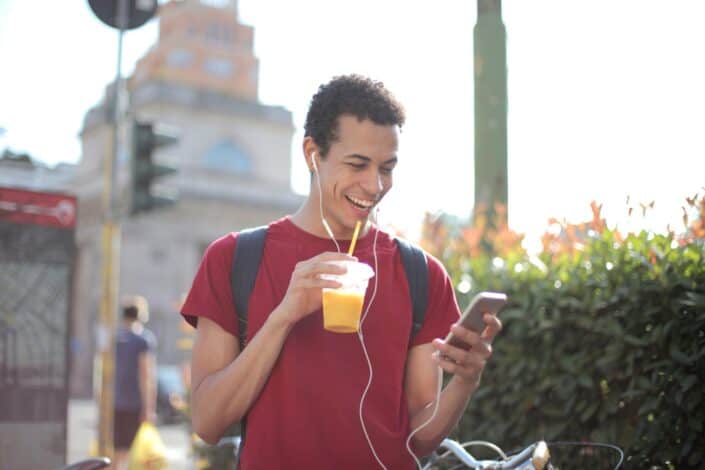 cheerful-man-with-smartphone-drinking-juice-on-street-