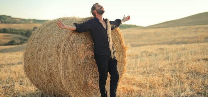 man-standing-by-hay-bale-in-field