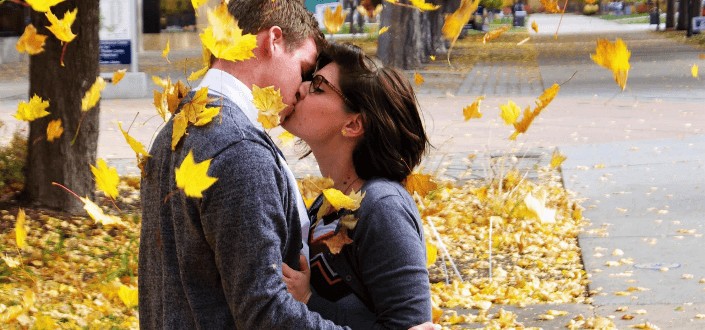 Couple kissing underneath a maple tree with leaves falling