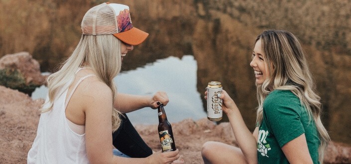 Two women drinking beer near the river