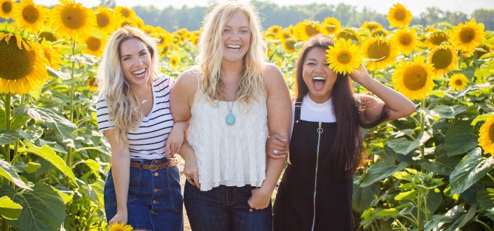 Three girls smiling in a sunflower field