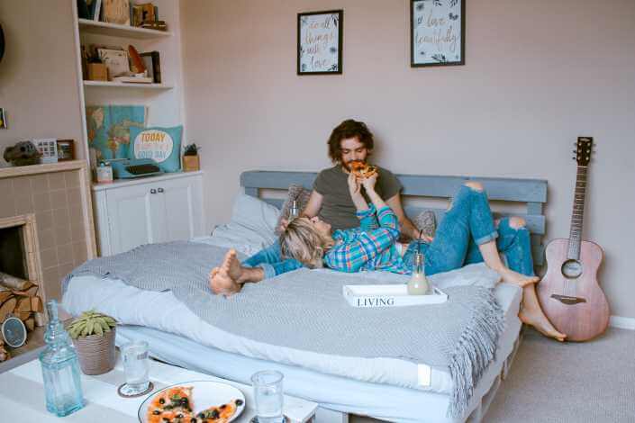 Couple cozy in bed and eating pizza