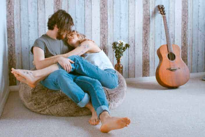 Couple cozying up on a bean bag with a guitar leaning on the wall beside them