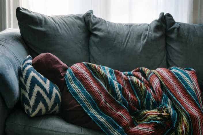 Sick person lying on sofa with blankets