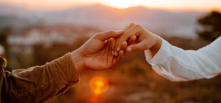 unrecognizable-couple-holding-hands-at-sunset-