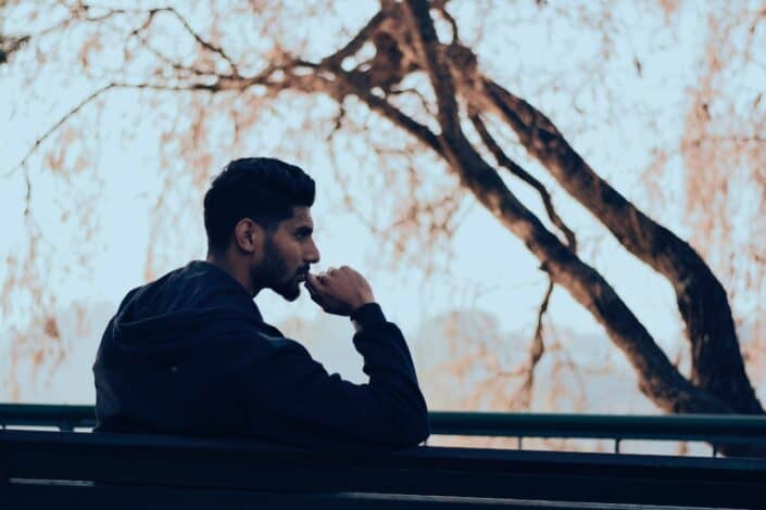 man-in-black-hoodie-sitting-on-bench-near-green-trees-