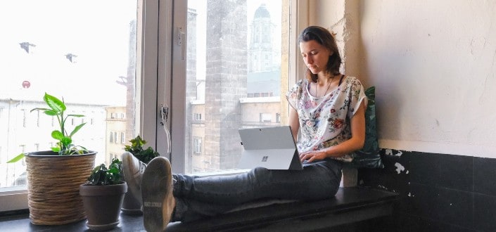 Woman Sitting on a Ledge Working on Her Tablet