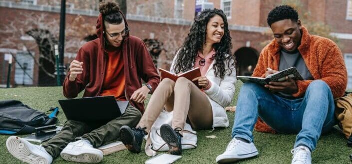 cheerful-multiethnic-students-with-books-sitting-near-university-