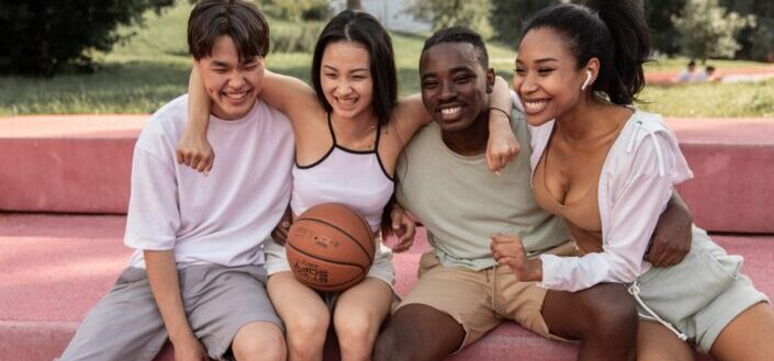 happy-multiracial-friends-embracing-on-bench-after-basketball-training-