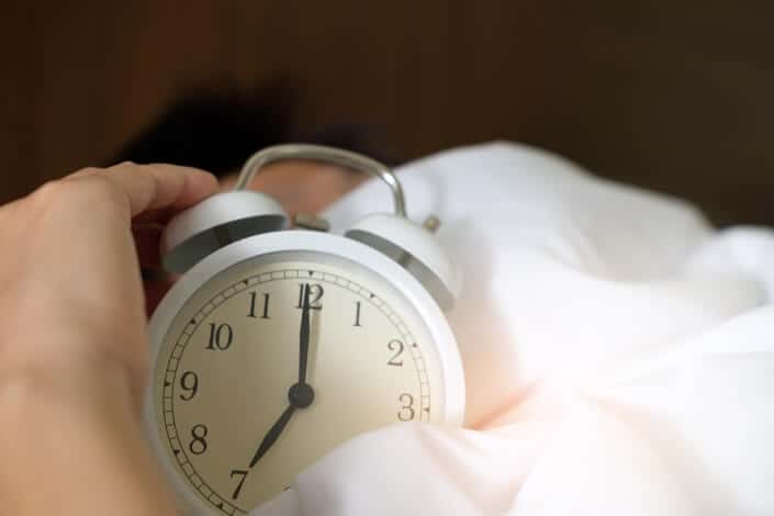 An alarm clock being held while sleeping.