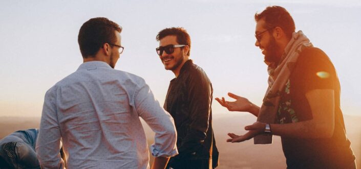 Three male friends talking about something while outdoors.