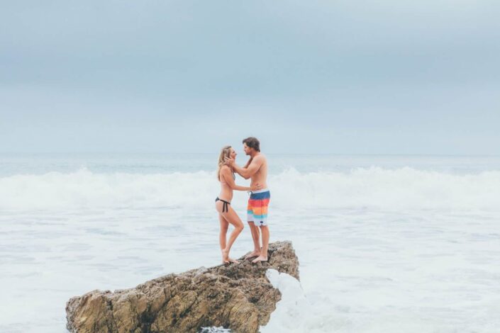 Couple standing for a phot on a cliff in the middle of strong waves