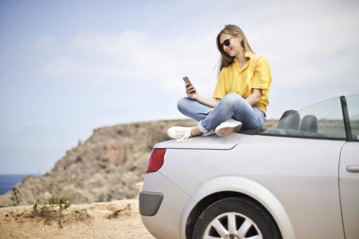 Girl sitting on top of car and reading her text