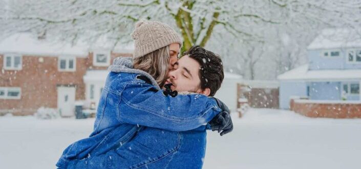 A man carrying a woman that is kissing him while it's snowing