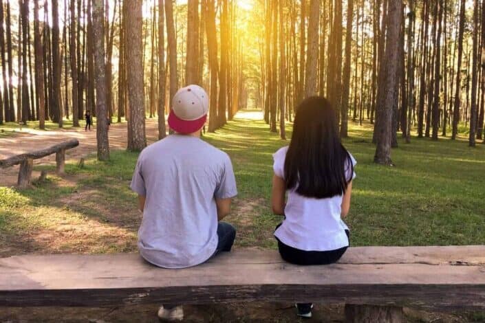 Man and woman talking facing the woods.