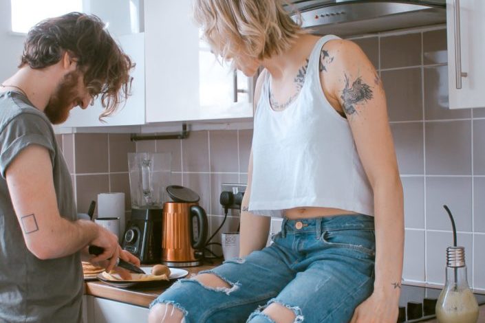 tattooed woman looking at man preparing food