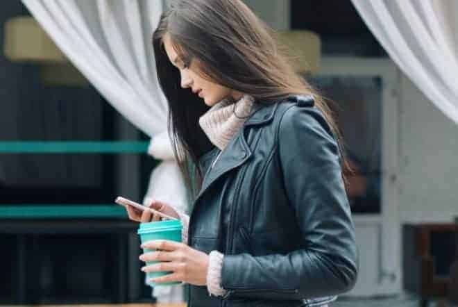 Girl carrying coffee looking down to text - Questions To Ask A Girl Over Text