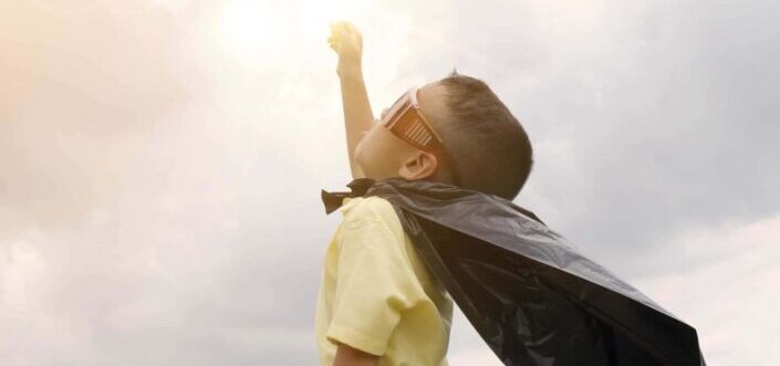 A cute kid wearing a plastic bag as his cape imagining to fly like a superhero