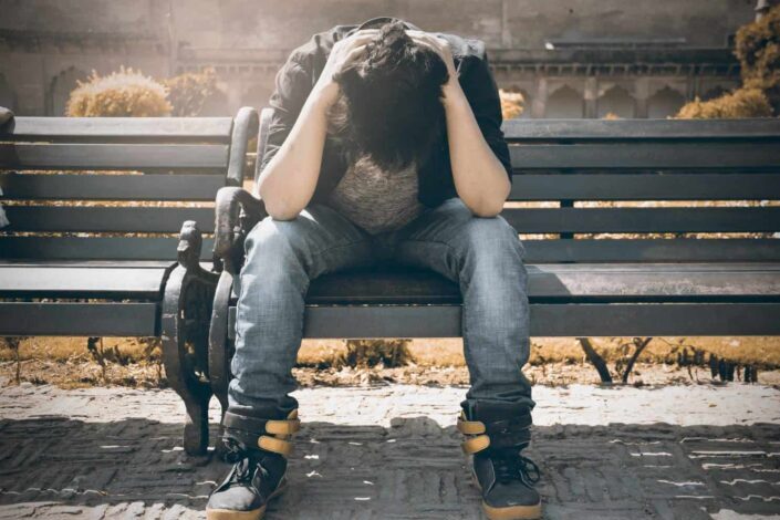 Man seated on bench clutching his head