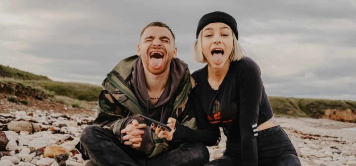 Silly couple on a pebbled beach, making wacky faces. 