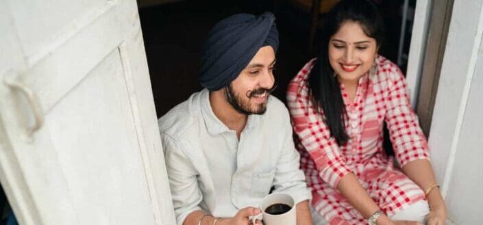 Couple sitting by the doorway, talking while the guy is having coffee.