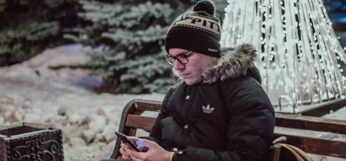 Guy sitting on a park bench and browsing his phone.