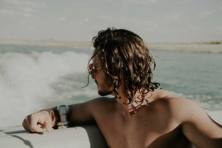 long haired man sitting by the sea