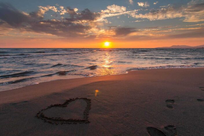 A heart on the sand with a beautiful sunset view.