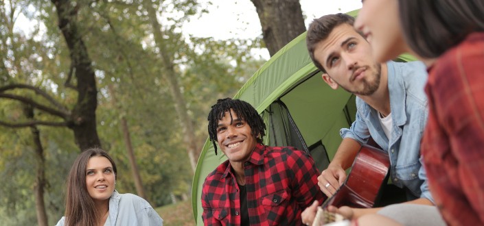 man playing guitar while camping with friends