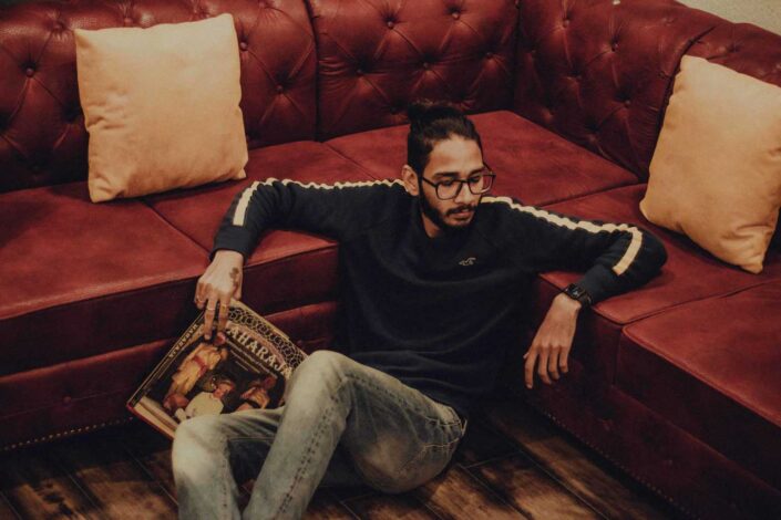 Guy holding a magazine while sitting on the floor and leaning against a leather couch