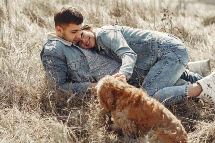 Happy couple with dog lying on dry grass