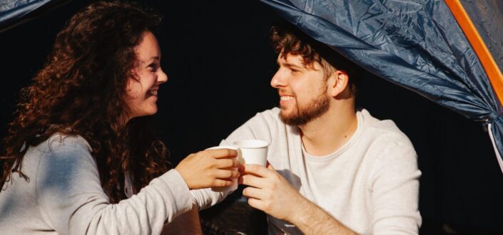 cheerful-couple-of-travelers-with-coffee-talking-in-tent-