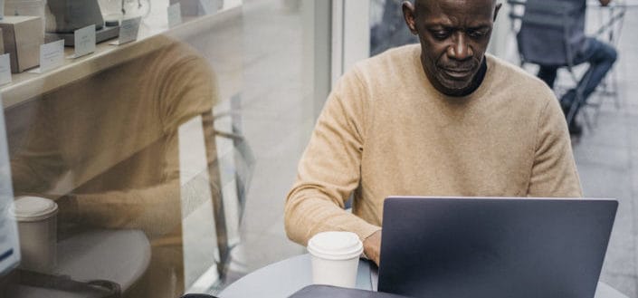 A man wearing nude sweater working on his laptop outside the coffee shop