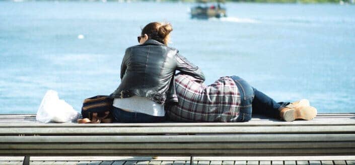 man lying on a woman's lap at the side of a body of water