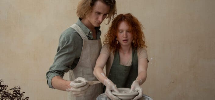 man standing next to a woman making pottery