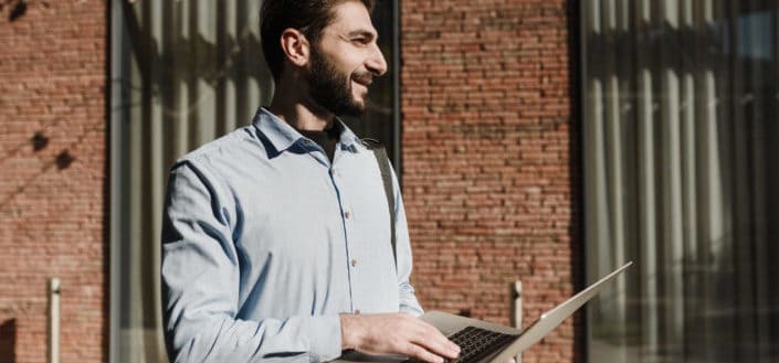 man smiling while holding his laptop