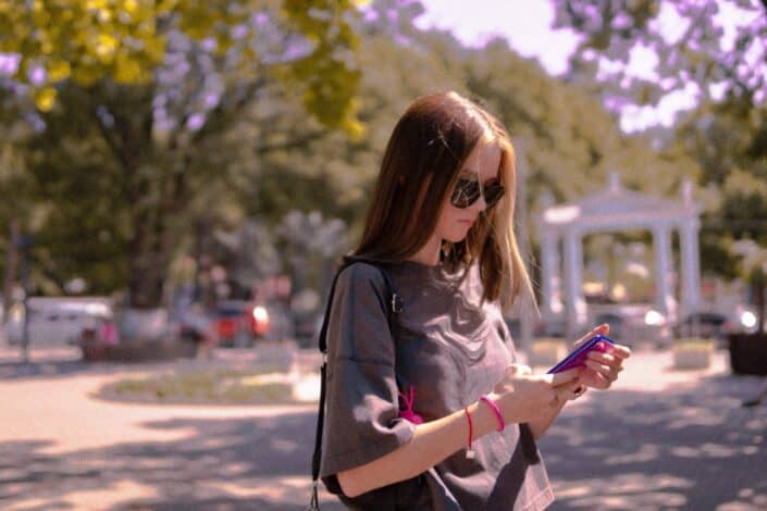 A lady with sunglasses, texting while outdoors.