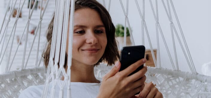 Girl sitting in a white swing smiling at her phone.